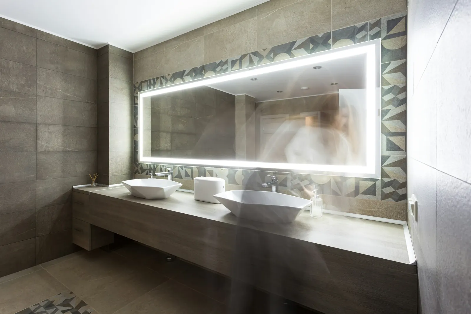 A modern washroom with two sinks and a lit mirror